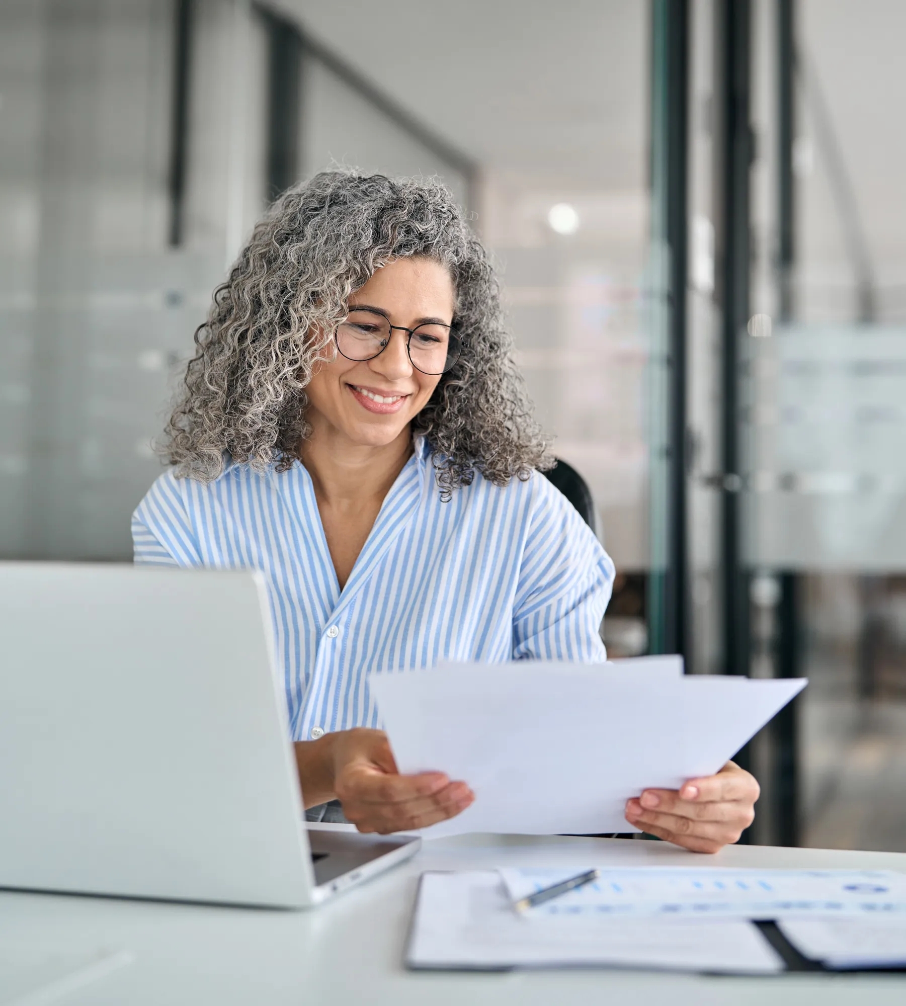 A woman sitting at a computer and reading a piece paper