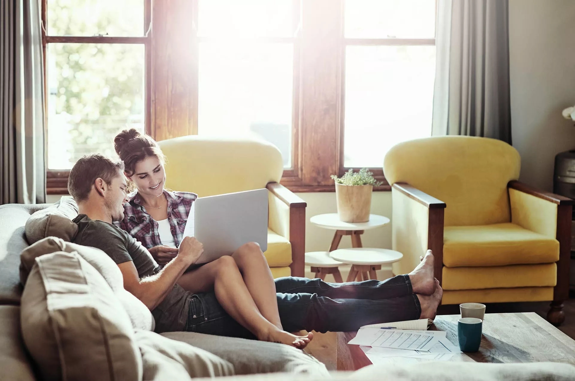 A couple sitting on a couch, viewing a laptop.