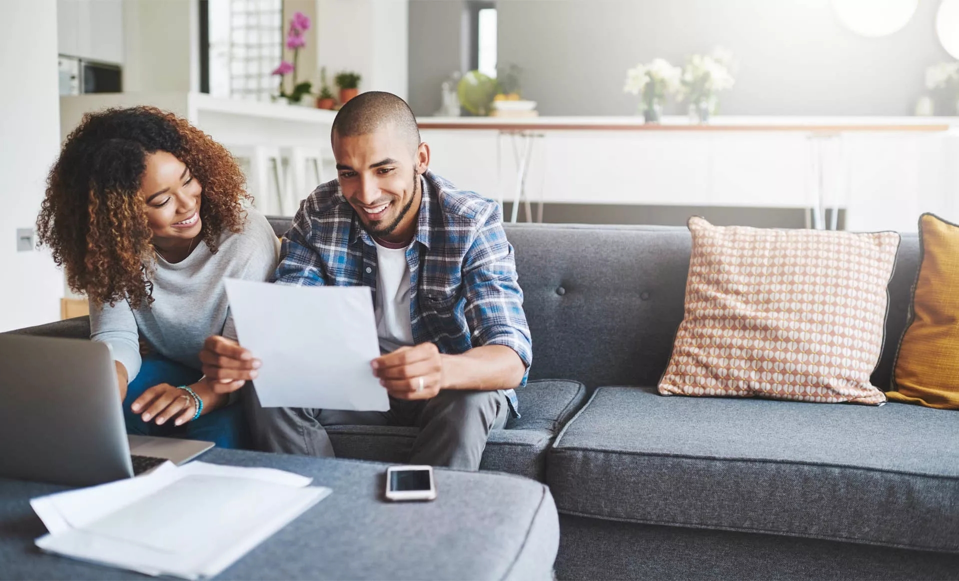 A couple sitting on their couch in the living room smiling over papers in their hands.