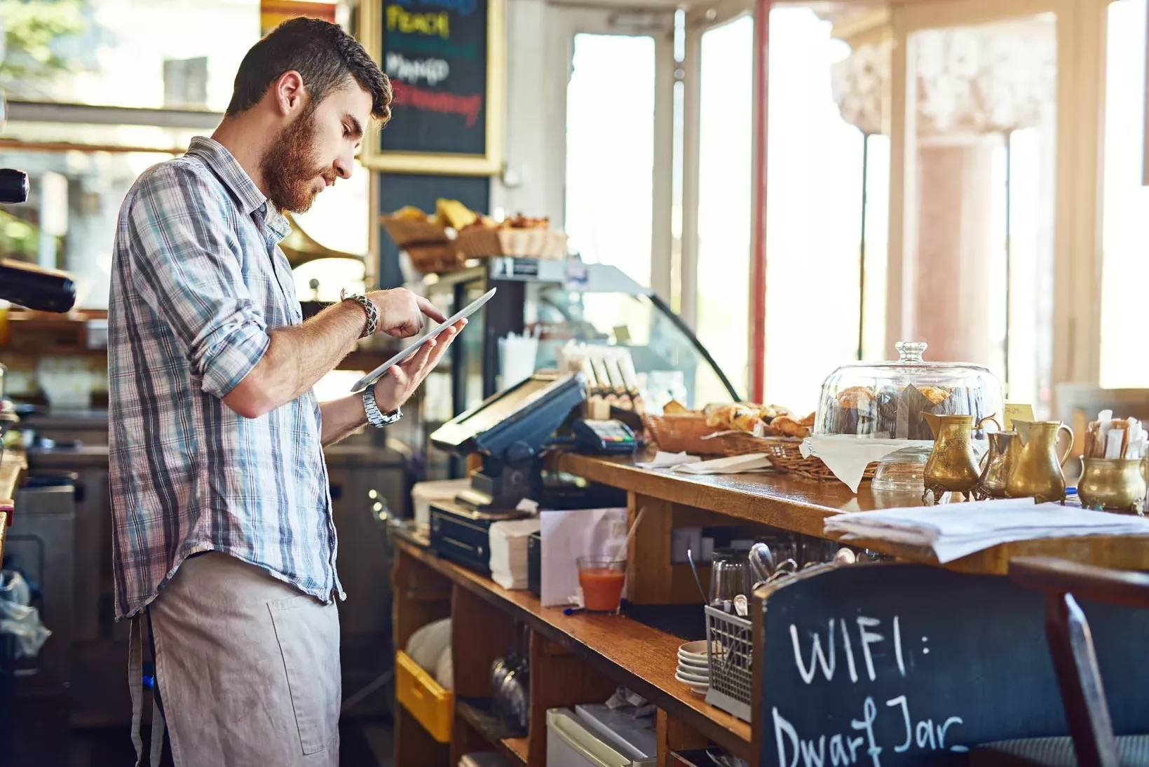 A coffee shop owner working on tablet behind counter