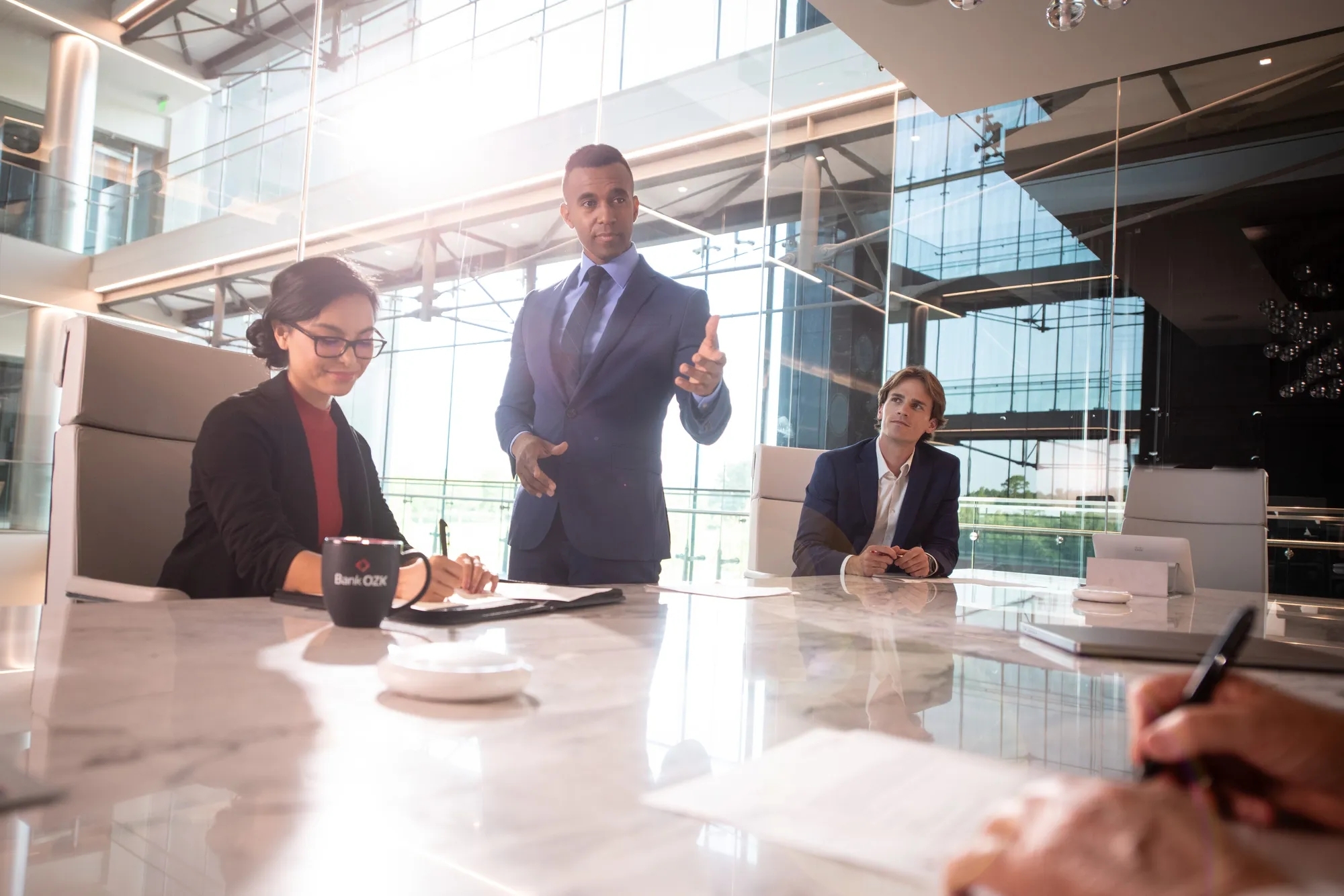 Three people in a meeting at a table discussing an open notebook on the meeting table between them.