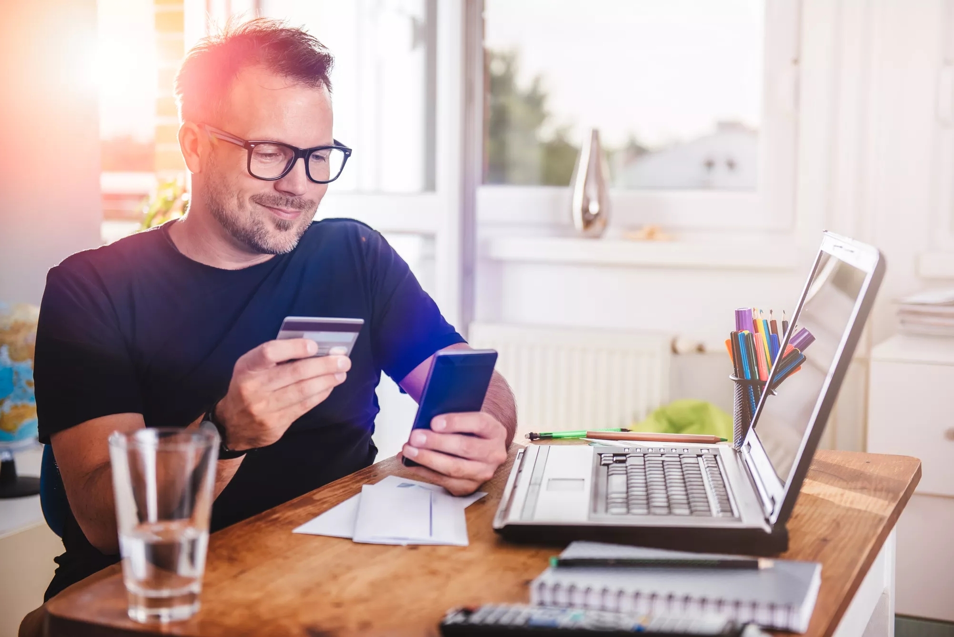 A person holding a debit card in one hand and mobile in another hand in front of a laptop.