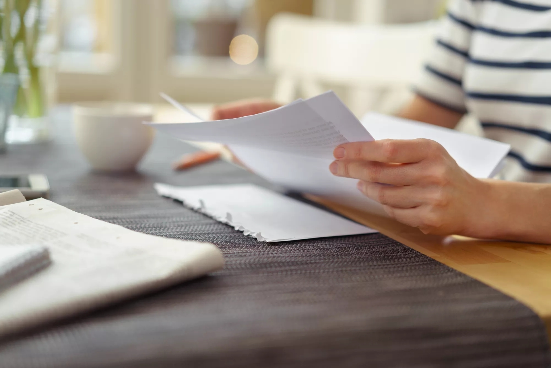 A person holding paper in their hand at a desk with more papers on it.