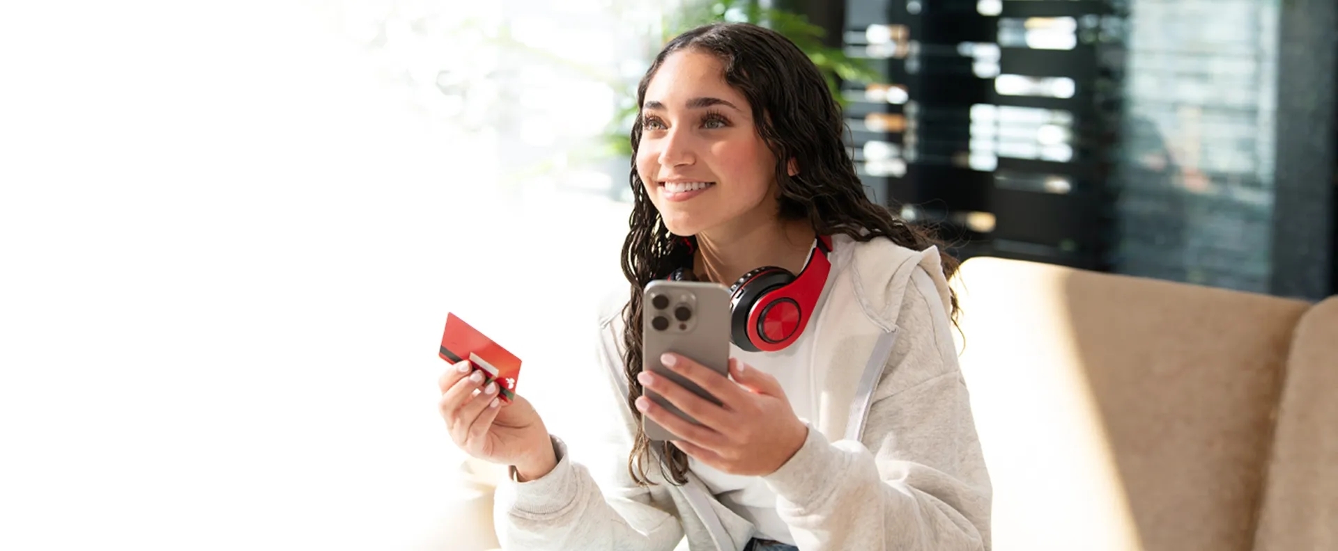 Young female sitting on a couch holding a phone in one hand and a credit card in her other hand. Young female sitting on a couch holding a phone in one hand and a credit card in her other hand.